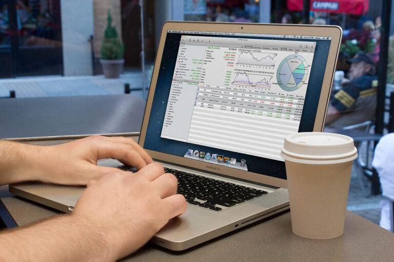 A laptop showing a stock portfolio dashboard with charts, next to a coffee cup